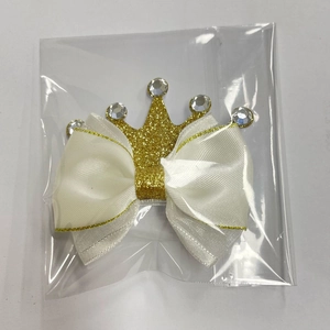Detail of white satin bow hair clip with gold crown and sparkling rhinestones