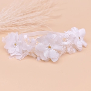 Détail d'un bandeau en dentelle blanche pour bébé avec fleurs 3D et perles dorées