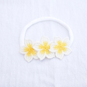 Detail of three white embroidered flower patches on a soft nylon baby headband