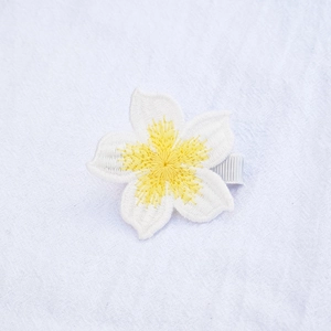 Close-up of handmade white knit flower hair clip with yellow center on a nylon band