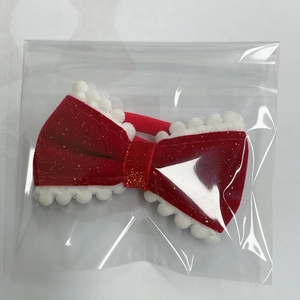 Detail of red velvet hair bow with gold glitter and white pom-poms in packaging