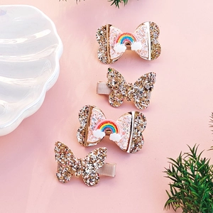 Detailed view of four golden glitter butterfly and rainbow bow hair clips on pink background