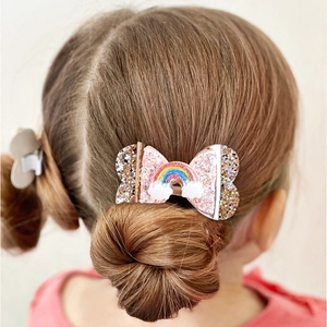 Close-up of glitter bow hair clip with rainbow and cloud detail on a girl's hairstyle