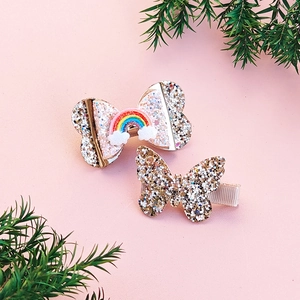 Detail of glitter bow hair clips for girls with rainbow charms on pink background