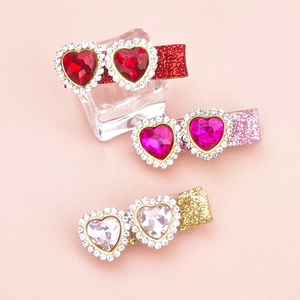 Three glittering rhinestone heart hair clips in red and pink displayed on ice props