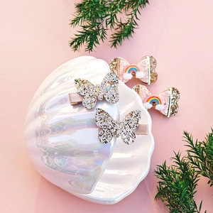 Close-up of glittery butterfly hair clips and rainbow bow clips in an elegant shell display