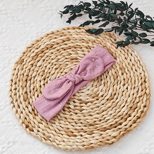 Detail of pink baby headband with gold polka dots and a bow on a woven mat