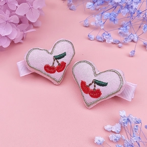 Detail of pink heart-shaped clips with cherry embroidery and gold trim for girls