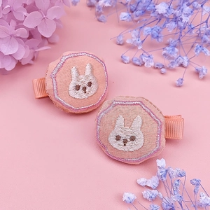 Close-up of pink fabric hair clips with embroidered white rabbit on a pastel background