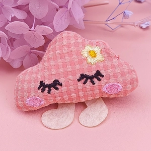 Detail einer Haarspange aus rosa Karostoff in Wolkenform mit besticktem Gesicht und Blume
