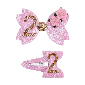 Detail of pink glitter bow hair clips featuring knit roses and gold number 2 for girls