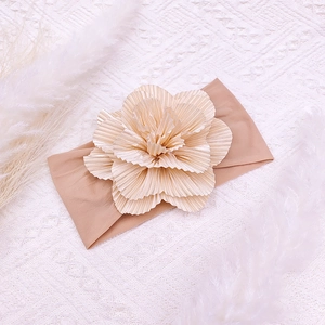 Detail of soft nylon baby headband with a large layered pleated flower on textured white rug