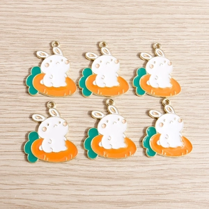 Detail of 6 enamel white rabbit and orange carrot pendants with golden loops on wood