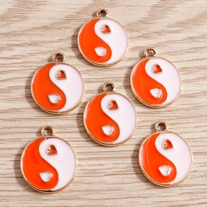 Detail of alloy yin yang heart charms with orange and white enamel on wood background
