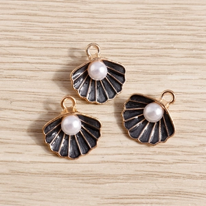 Detalle de colgantes de concha dorados con esmalte negro y perlas blancas centrales