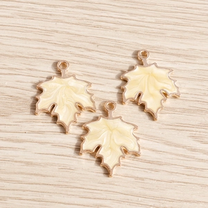 Macro shot of maple leaf charms with pearlescent white enamel and gold metal edges