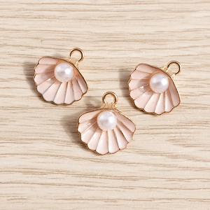 Detalle macro de tres colgantes de concha en esmalte rosa con perlas sobre madera
