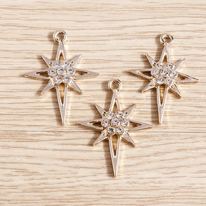 Trois pendentifs étoile dorés avec zircons posés sur un fond en bois clair texturé
