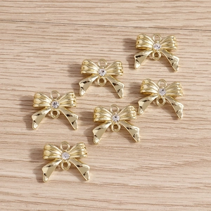 Pendentifs nœuds dorés avec strass et doubles boucles sur un fond en bois clair