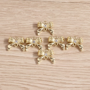Détail macro de six pendentifs nœuds dorés avec strass sur surface en bois clair