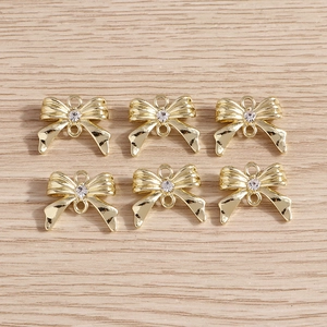 Vue détaillée de six pendentifs nœuds dorés avec strass sur un fond de bois clair