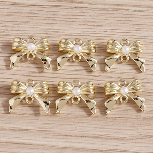 Détail de six pendentifs nœuds dorés avec perles blanches sur une surface en bois