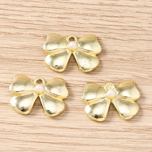 Close-up of golden bow pendants with imitation pearl centers on wood background