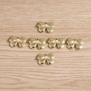 Detailed view of six golden bow pendants with pearls on a wooden surface for DIY jewelry
