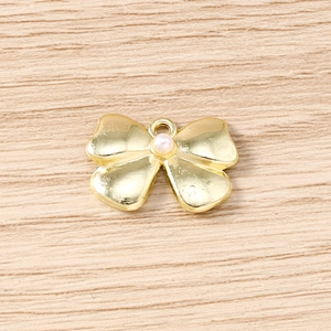 Macro detail of a golden bow pendant with pearl inlay and metallic texture for DIY jewelry