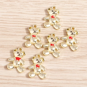 Detailed view of six gold alloy bear charms with red enamel bows on light wood surface