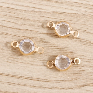 Golden double-loop crystal charms on wooden surface for DIY jewelry making