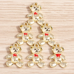 Detailed view of six golden alloy bear pendants with red bows on a light wooden background