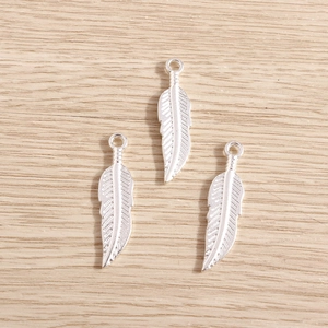 Silver plated feather leaf pendants for DIY jewelry making on a light wood background