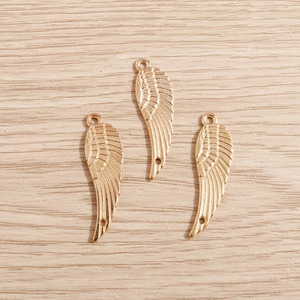 Vue détaillée de trois pendentifs ailes d'ange dorés avec textures de plumes sur bois