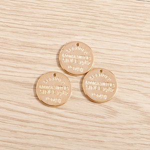 Detailed macro view of three round gold-plated geometric pendants with stamped letters
