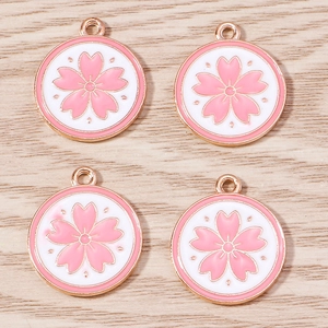 Detail showing four pink cherry blossom alloy charms with rose gold edges on wood surface