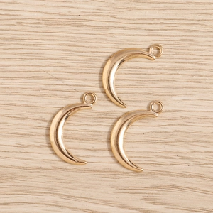 Detailed macro view of three gold-plated crescent moon charms on a light wood surface