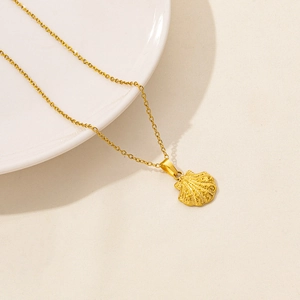 Dettaglio di una collana con ciondolo a conchiglia dorata con texture fini su sfondo beige