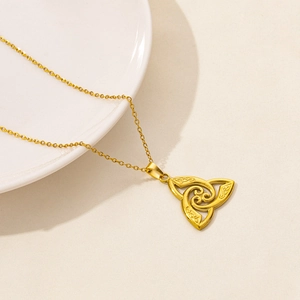 Dettaglio della collana con nodo celtico dorato e spirale su un piatto di porcellana bianca