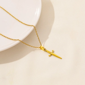 Dettaglio della collana con ciondolo a pugnale dorato su sfondo in ceramica bianca pulita