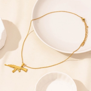 Dettaglio di una collana dorata con pendente a fucile su un vassoio di ceramica bianca