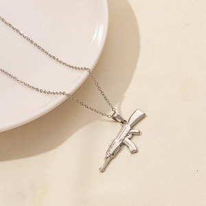 Dettaglio della collana con ciondolo a forma di fucile in acciaio inox su sfondo beige