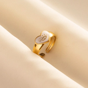Detail of gold evil eye heart ring with white enamel on cream silk background