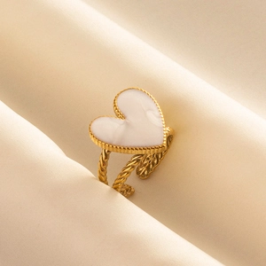 Détail macro d'une bague cœur vintage dorée avec émail blanc et anneau torsadé