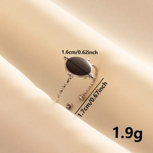 Détail d'une bague ovale en émail noir avec bord perlé sur un tissu en soie beige