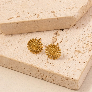 Detailaufnahme goldener Sonnenblumen-Ohrstecker mit matter Textur auf Naturstein