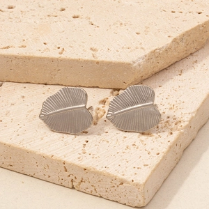Detail von blattförmigen Edelstahl-Ohrsteckern mit feiner Aderstruktur auf Steinplatten