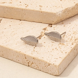 Makro-Detail von silbernen Blatt-Ohrsteckern auf Stein mit feinen Blattader-Mustern
