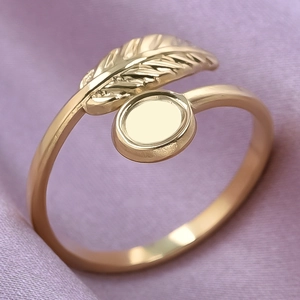 Detailed view of a gold leaf feather ring with oval bezel setting on purple silk