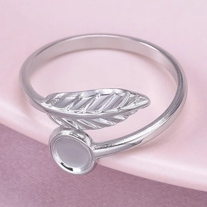 Macro shot of silver leaf-shaped ring with brushed metal texture on pink surface